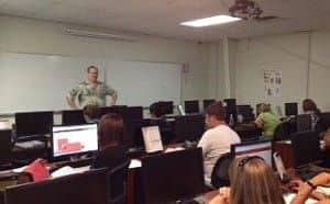 A man standing at the front of a classroom full of students at computers