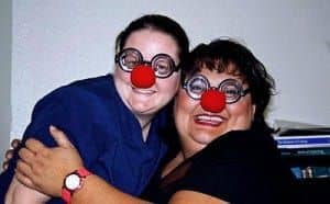Two woman smiling with red clown noses on their faces
