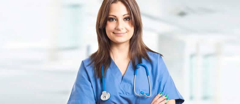 Close up of a medical professional, smiling with arms folded in a hallway of a medical establishment.