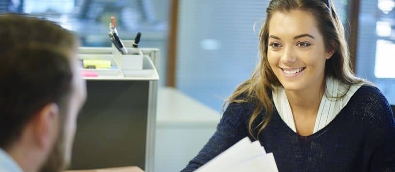 Woman smiles at man across from her at desk in an office setting.