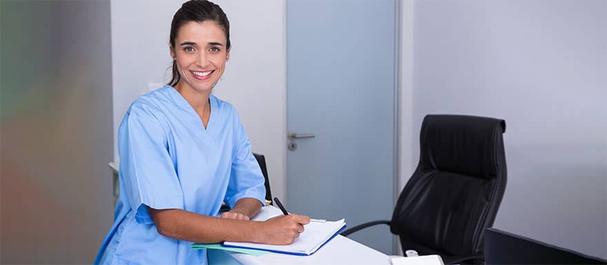 Female medical assistant writing notes at a desk.